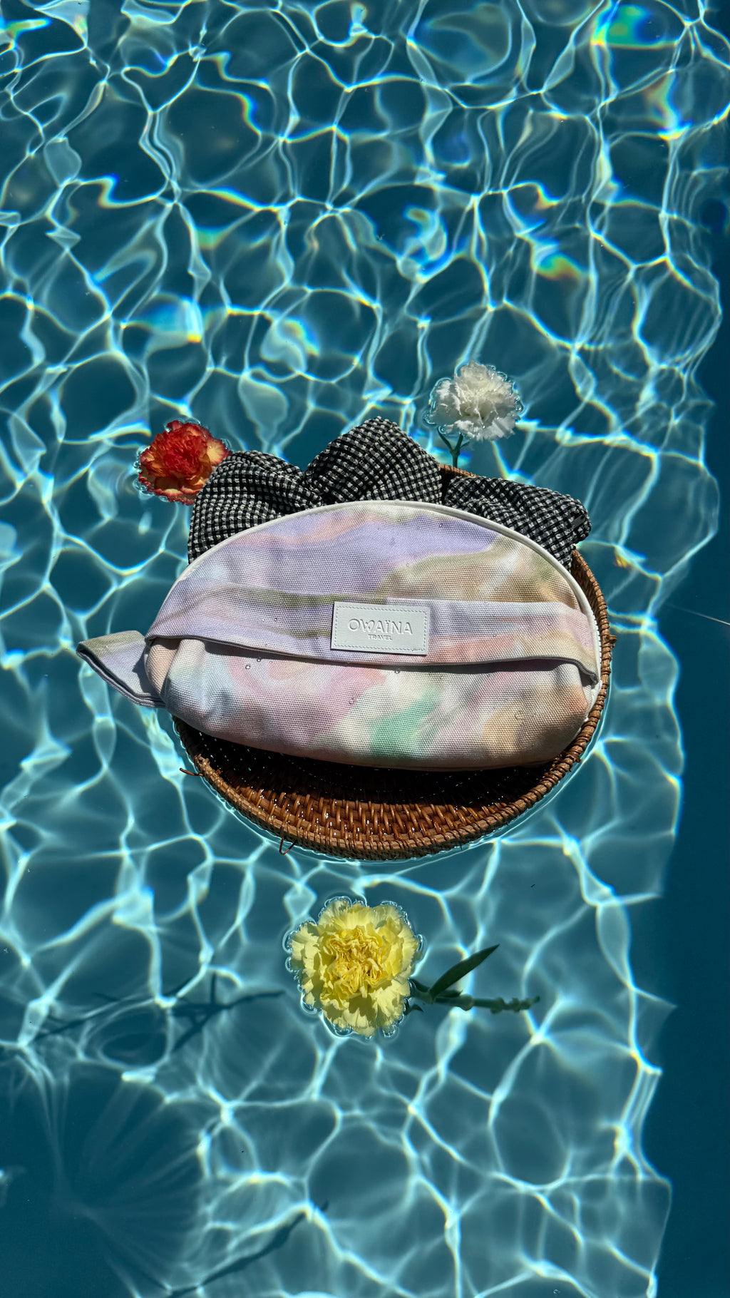 Trousse à maillot de bain fermé. Tissu déperlant. Présenté sur un plateau en osier flottant au dessus d’une piscine avec des fleurs.