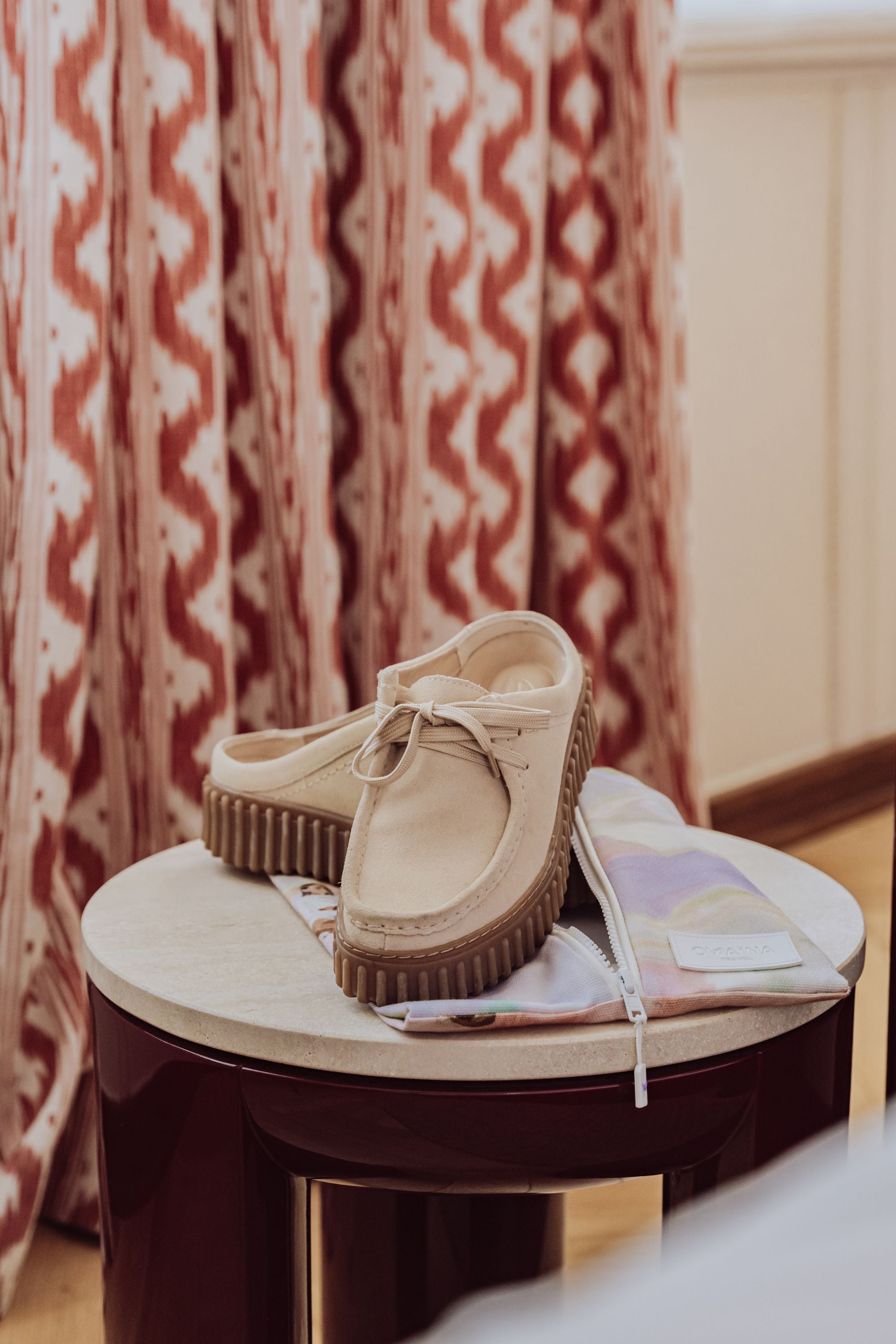 Chaussures beige avec pochette de rangement à chaussures Owaïna sur table ronde dans hôtel boutique.