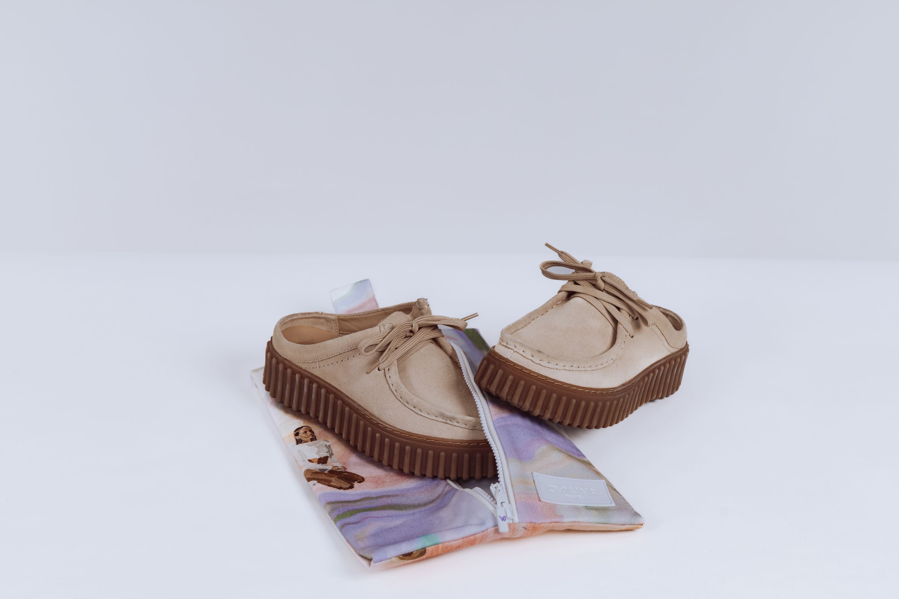 Paire de chaussures beiges posées sur une housse à chaussures zippée Owaïna pastel marbrée sur fond blanc.