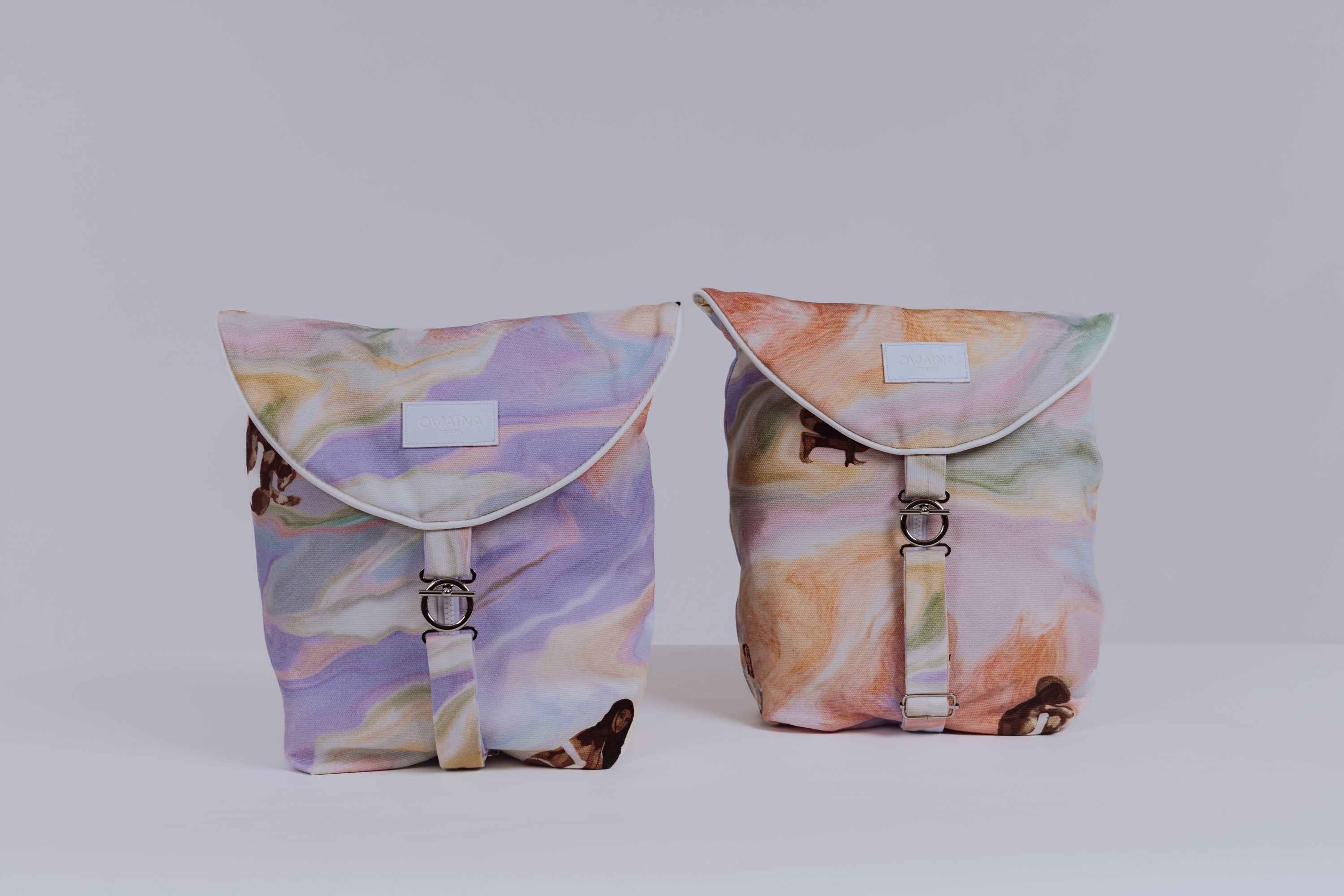 Duo sacs à vêtements de voyage Owaïna pastel avec rabat arrondi et fermoir métallique argenté, présenté en duo sur fond blanc minimaliste.