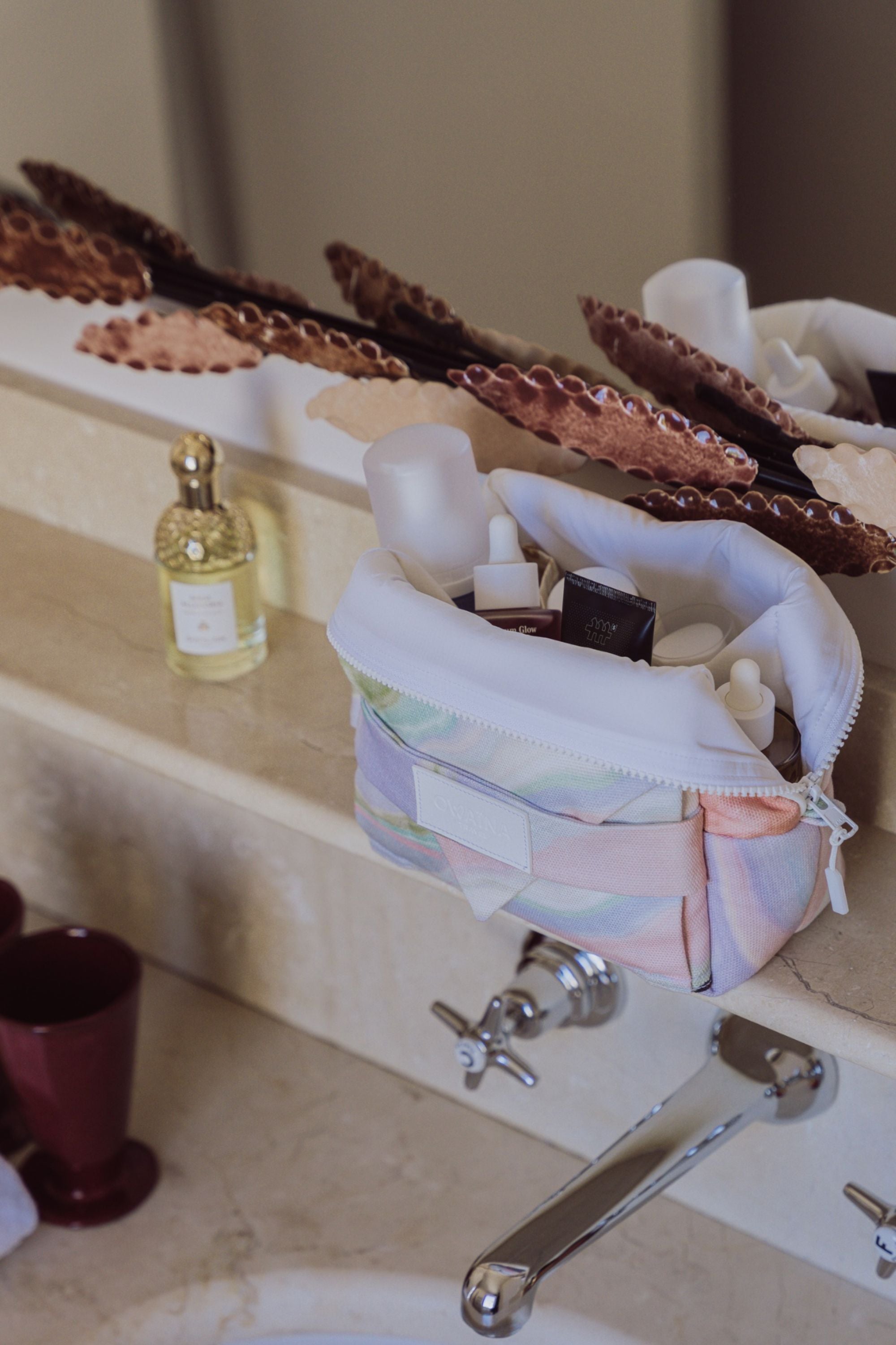 Trousse de toilette à compartiments Owaïna pastel ouverte avec produits de beauté dans une salle de bain élégante et.