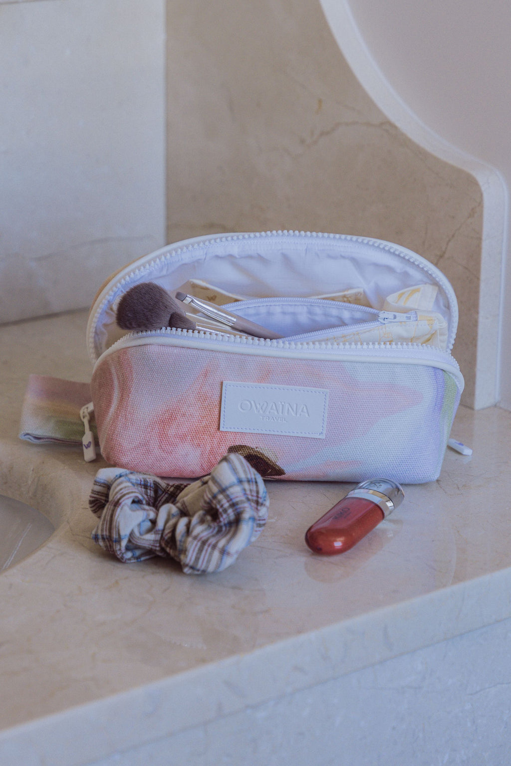 Gros plan sur une trousse à maquillage beauté Owaïna rose pastel avec pinceaux et produit cosmétique sur marbre beige.
