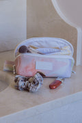 Gros plan sur une trousse à maquillage beauté Owaïna rose pastel avec pinceaux et produit cosmétique sur marbre beige.