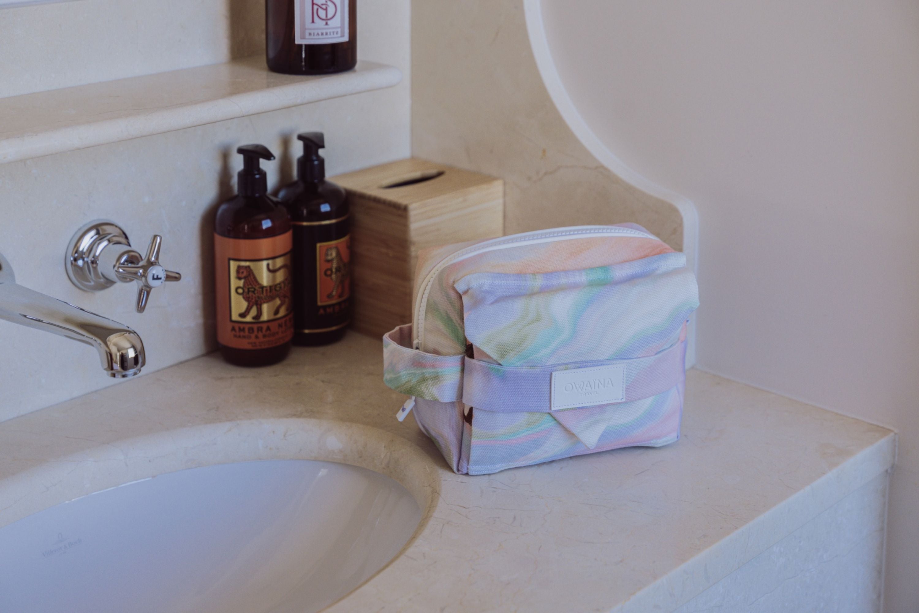 Trousse de toilette à compartiments Owaïna pastel dans une salle de bain d’hôtel élégante.