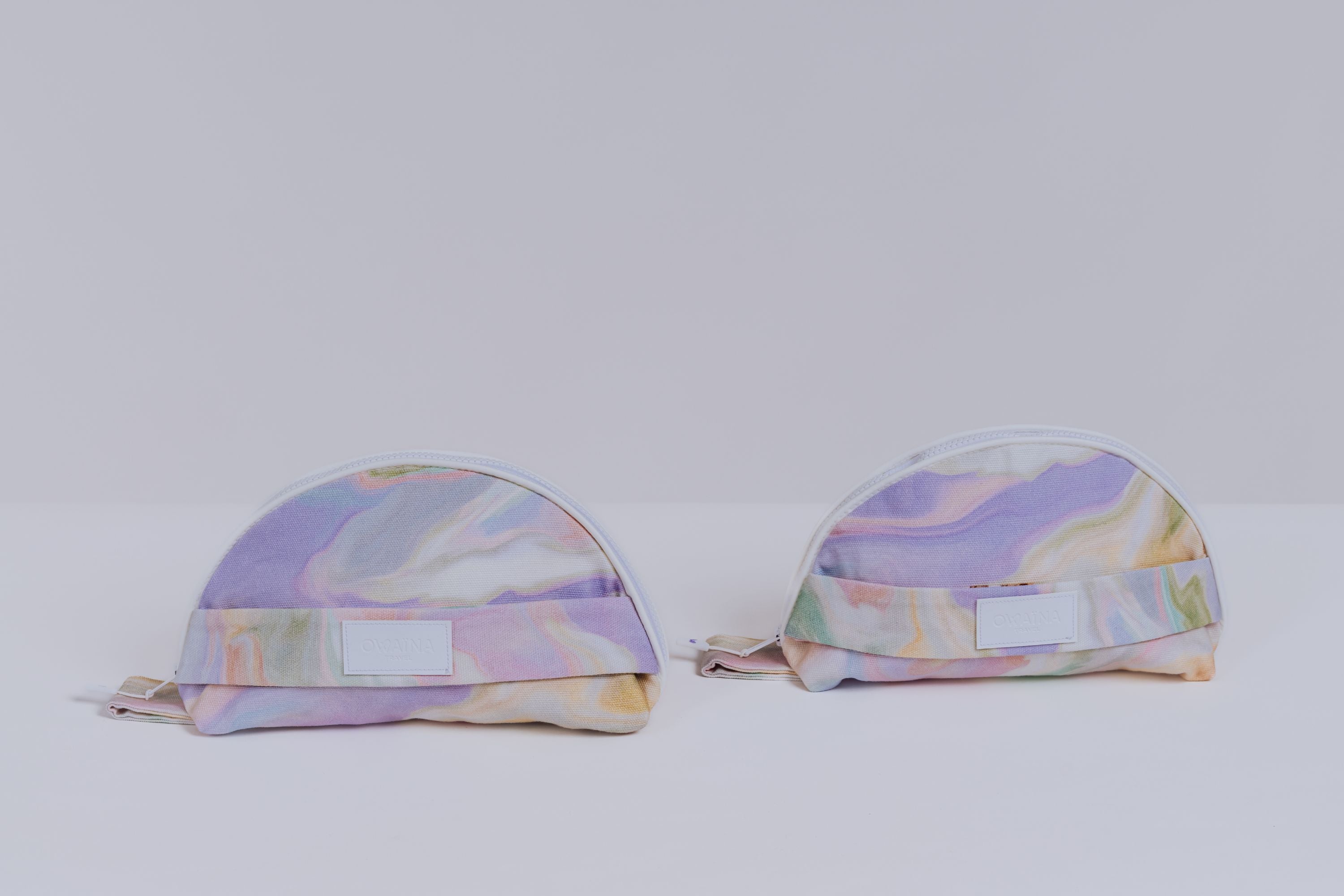Deux trousses à maillots de bain Owaïna pastel marbrées avec fermeture zippée blanche et détails minimalistes.