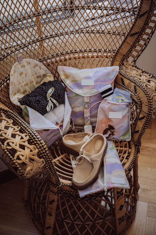 Pack de quatre accessoires de voyage pour ranger vêtements, lingerie, chaussures. Placés sur une chaise en rotin dans un hôtel luxueux et lumineux.