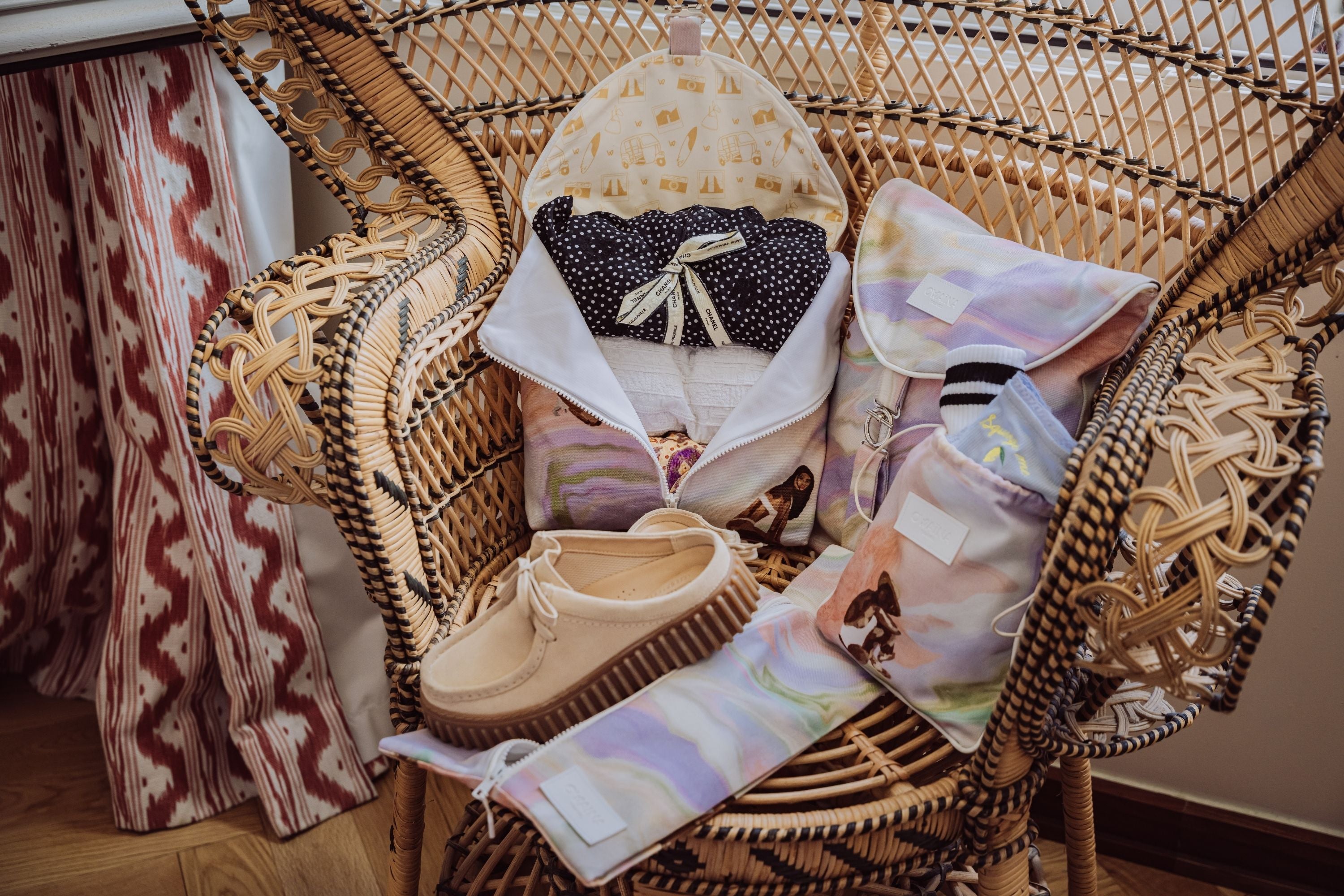 Pack de quatre accessoires de voyage pour femme. Pour organiser sa valise avec des accessoires pour y mettre ses vêtements, lingerie, chaussures. Les accessoires sont disposés sur une chaise en rotin dans un hôtel boutique.