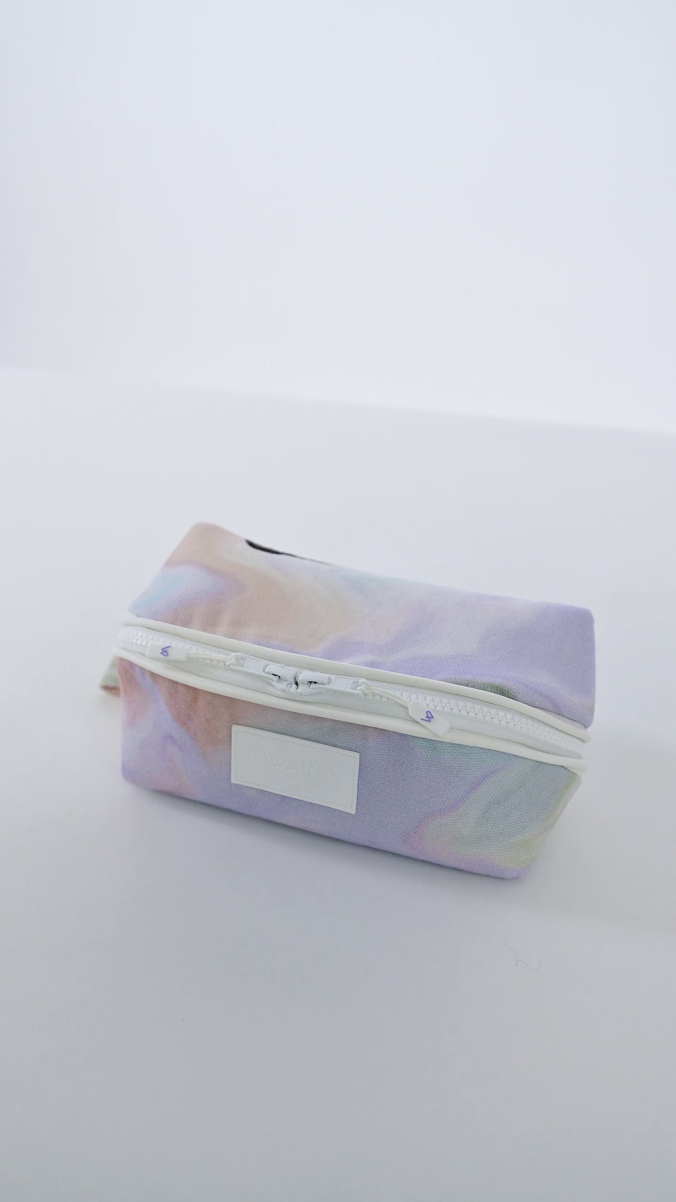 Vidéo trousse à maquillage avec compartiments Owaïna aux motifs pastel marbrés avec fermeture zippée blanche sur fond blanc.