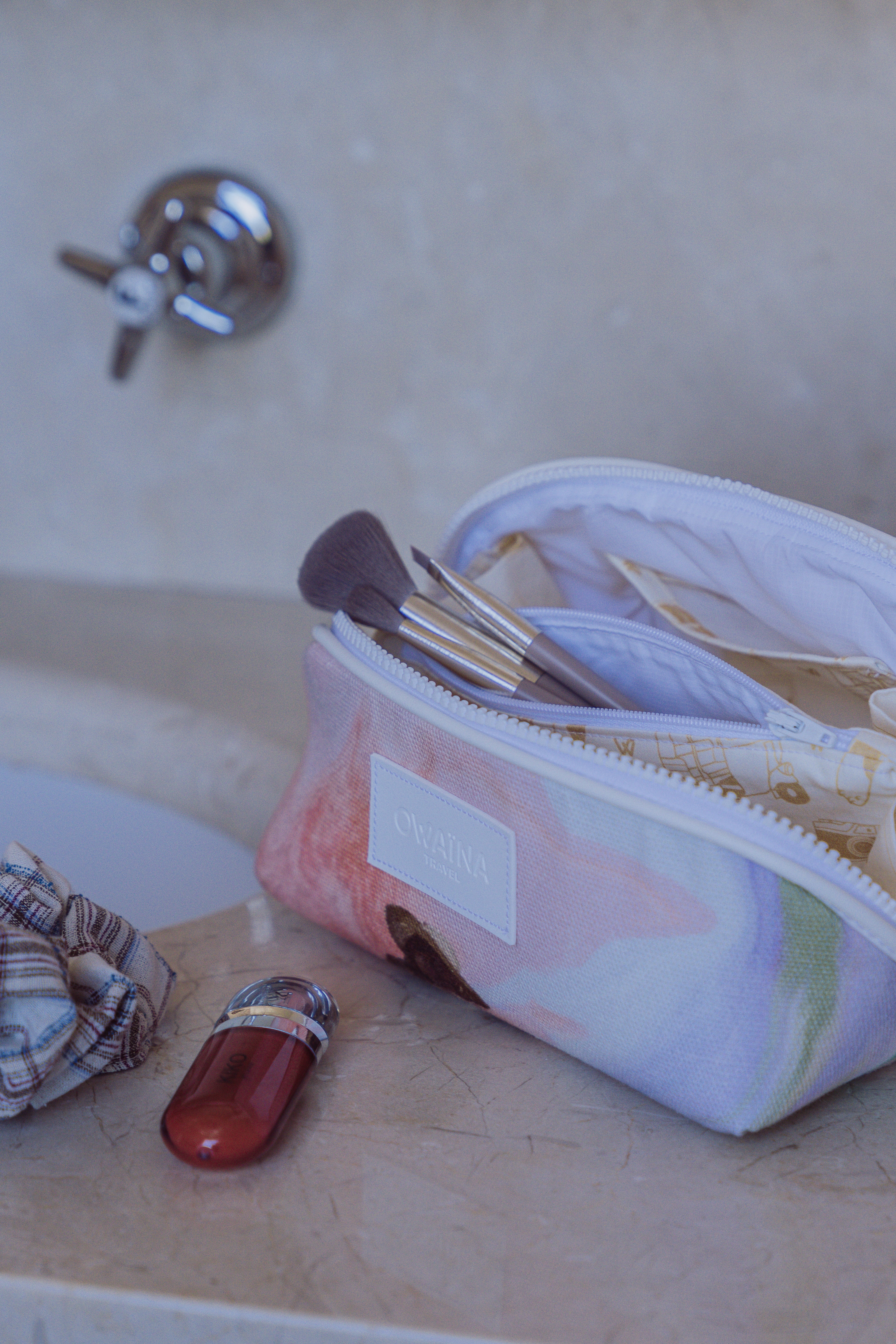 Trousse à maquillage à compartiments ouverte dans salle de bain luxueuse et lumineuse. Pour essentiels beauté en voyage.