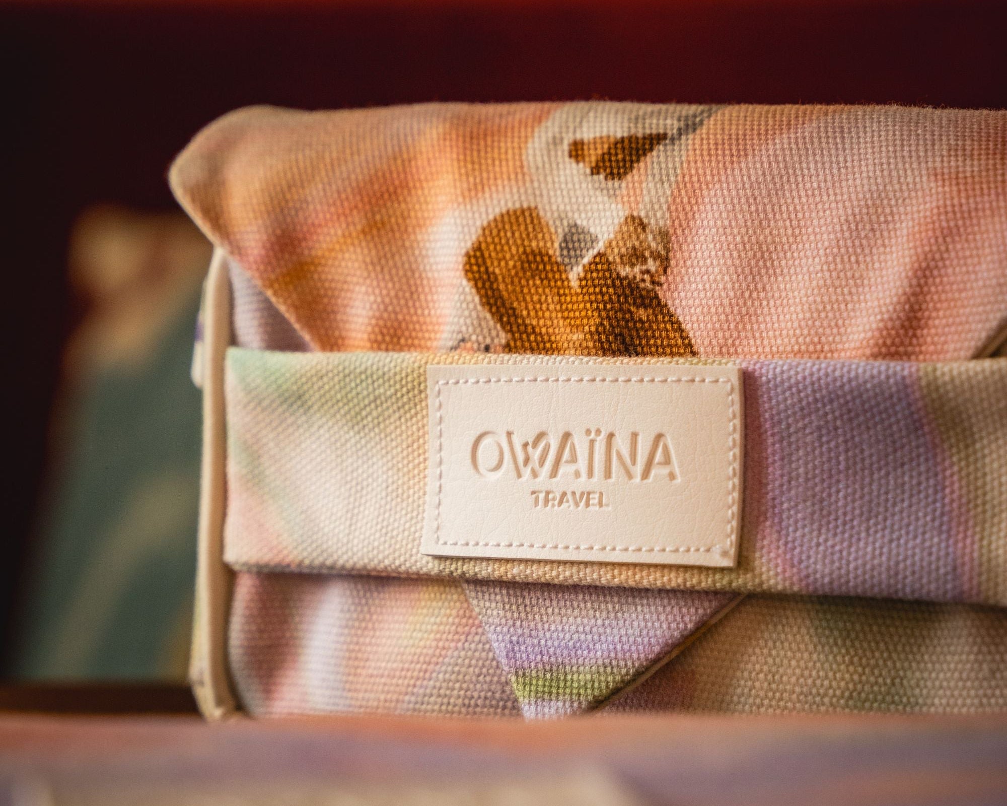 Zoom sur l'étiquette de marque d'Owaïna, de la trousse à chargeurs à double compartiments. Accessoire de voyage disposé sur un salon d'un hôtel boutique luxueux.